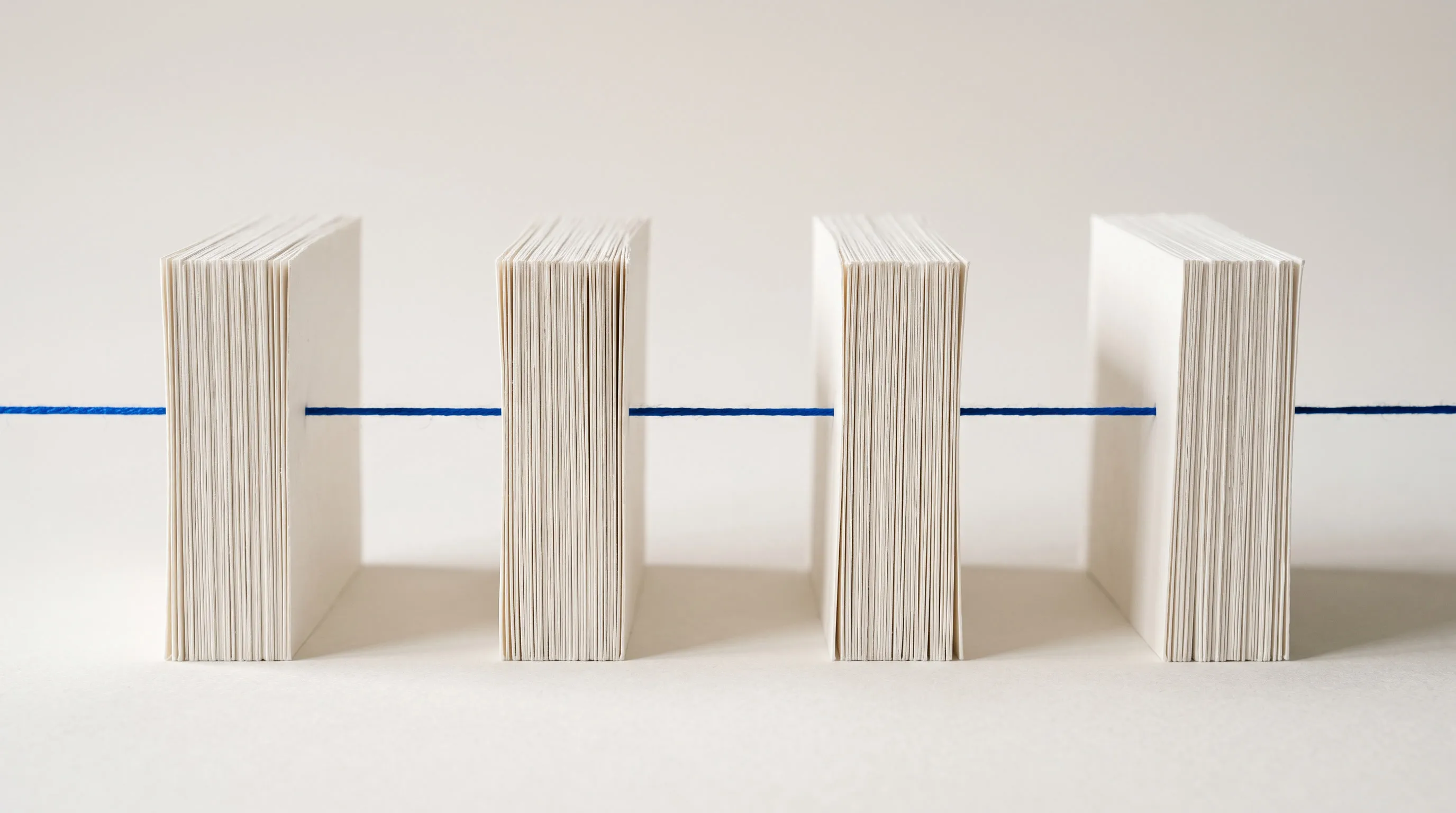 Four separate stacks of paper standing like columns, with one blue thread passing cleanly through the space between them